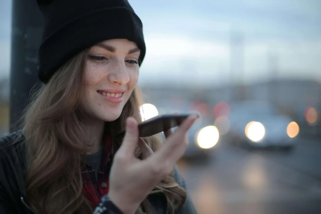 An individual holding a smartphone near their mouth, presumably using a voice search function, with blurred city lights in the background