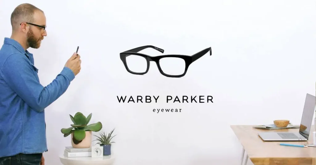 Man using smartphone to engage with Warby Parker eyewear branding, featuring glasses and a plant on a desk, illustrating DTC marketing strategies.